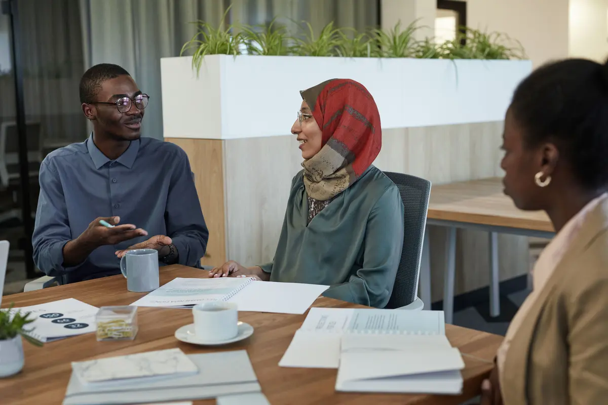 Three people talking across a table with papers and coffee